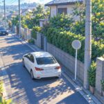中央線のない住宅街の道を十分な車間をあけて走る2台の車のイラスト